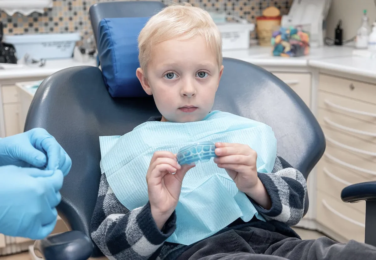 Blond boy in a dental chair holding a mouthguard