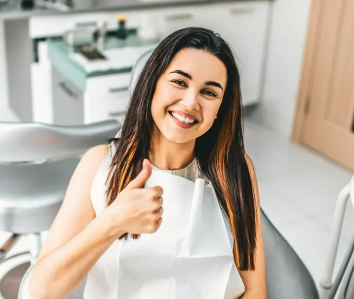Young woman smiling in a dental chair giving a thumbs up